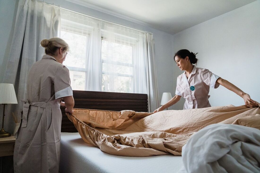 Cleaners making a bed in a sunny bedroom