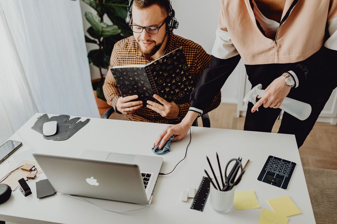 Cleaner wiping an office desk beside a laptop