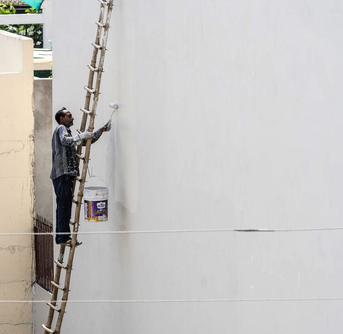 Painter on a ladder painting a tall exterior house wall