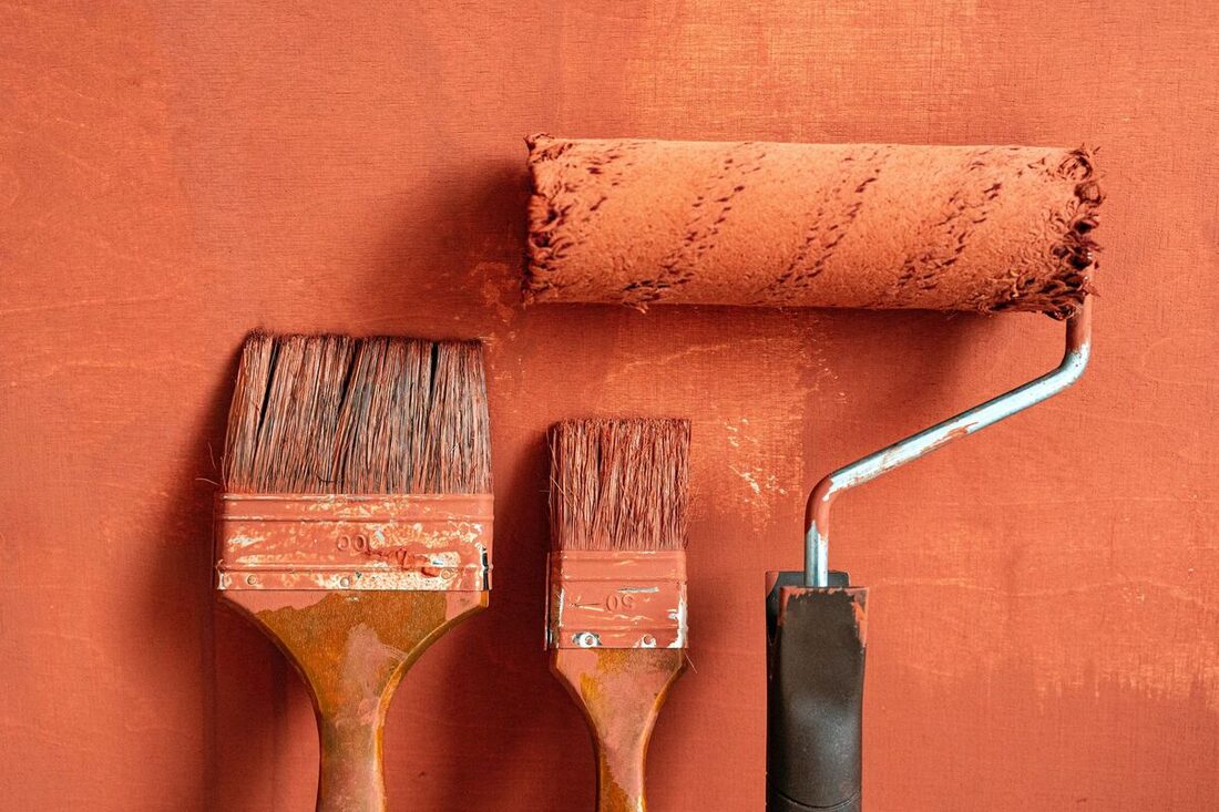 Painting brushes and roller against a freshly painted wall